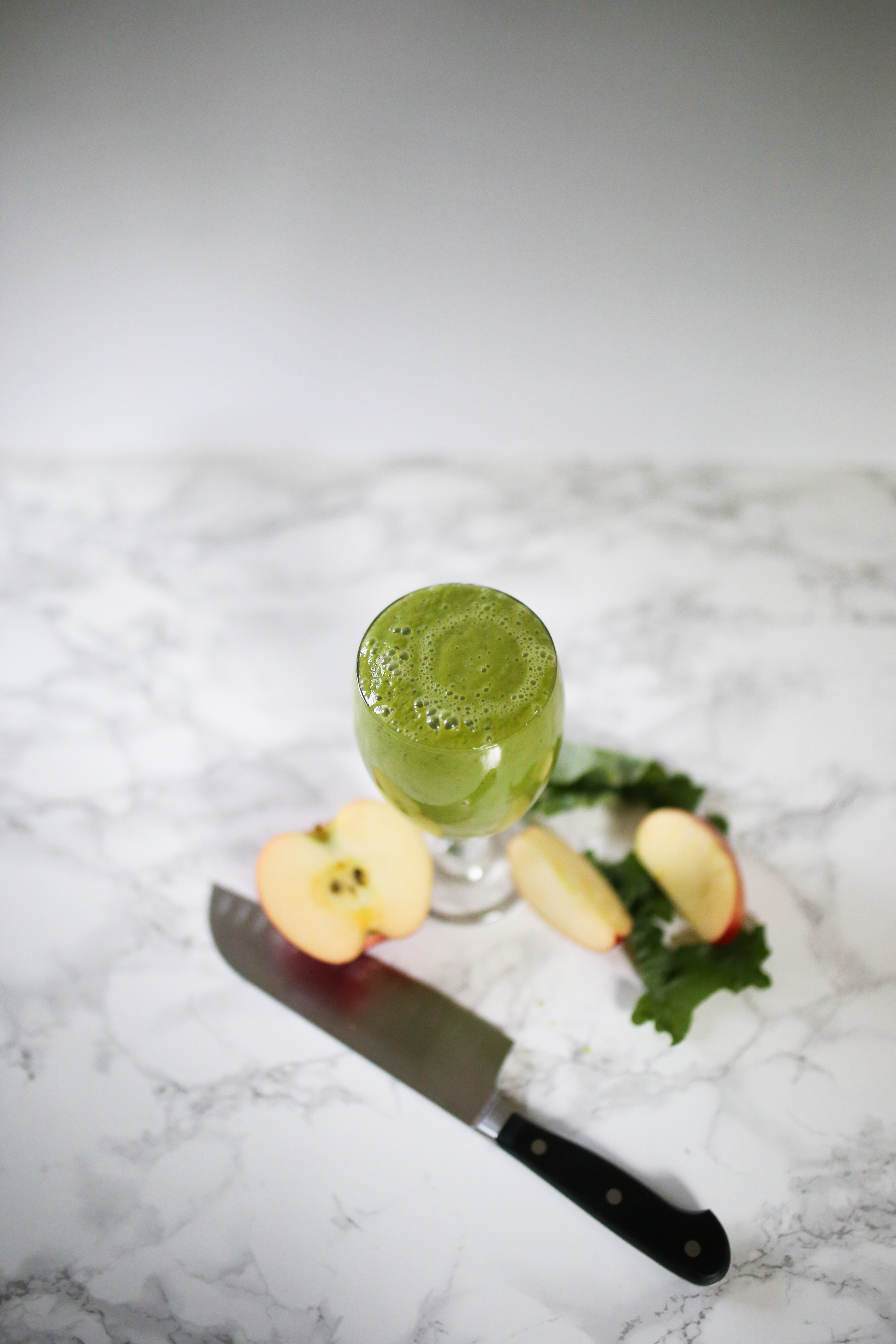 green pineapple apple smoothie in glass. Apples and knife on counter. Shot from above.