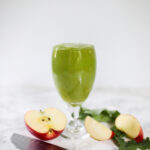 green pineapple apple smoothie in glass. Apples and knife on counter.