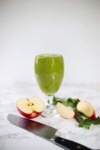 green pineapple apple smoothie in glass. Apples and knife on counter.