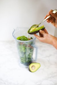avocado being added to green smoothie in blender