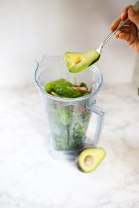 avocado being added to green smoothie in blender