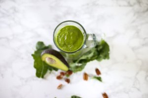 image from above green smoothie in glass. styled with avocado and kale.