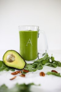 green smoothie in clear glass. Avocado laying beside drink.