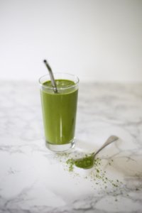 Green Matcha Maca smoothie in tall glass with metal straw, matcha on table with spoon