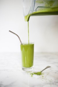 Green Matcha Maca smoothie in tall glass with metal straw, smoothie being poured from vitamix blender