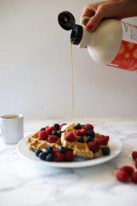 waffles the butter and berries on top, syrup being poured on top.